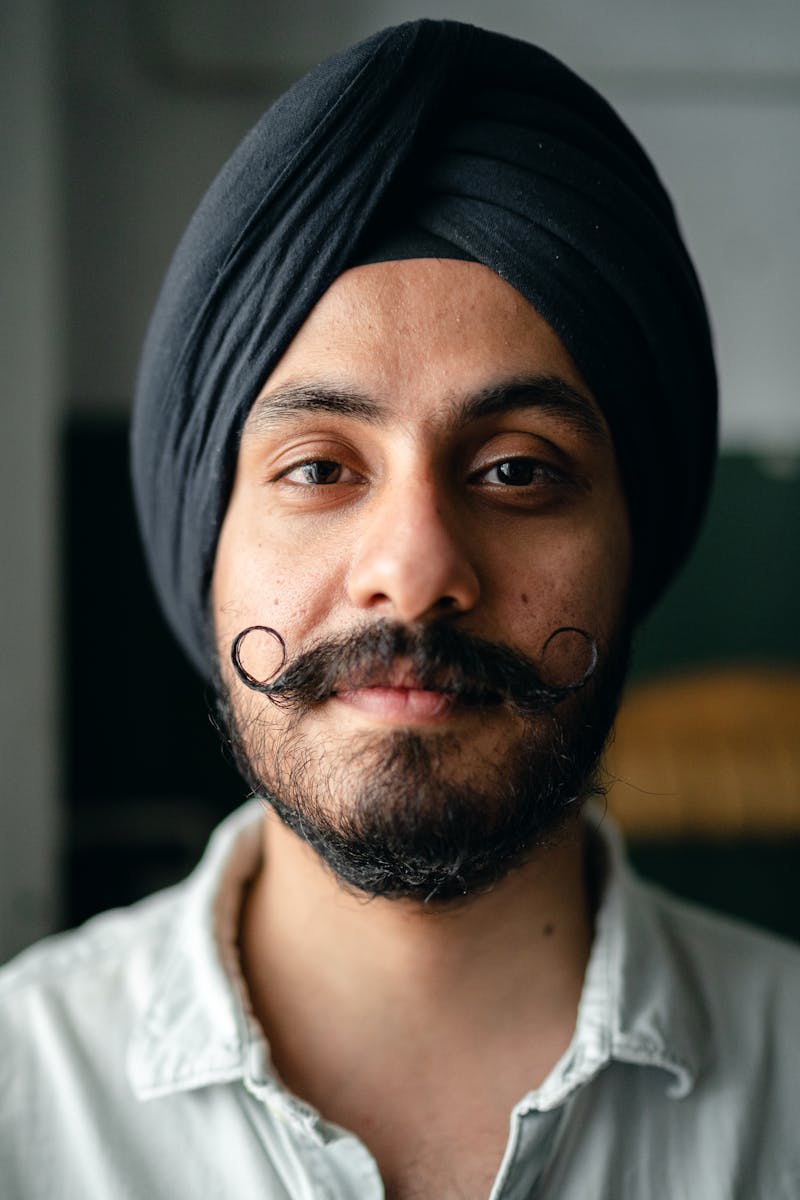 Close-up portrait of a confident young man wearing a turban and mustache, exuding style and individuality.