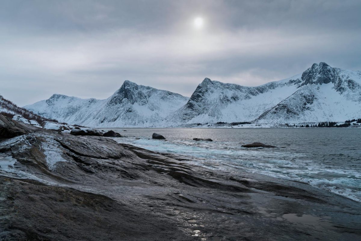 Serene snowy mountains and fjord in Norway under a winter sky.