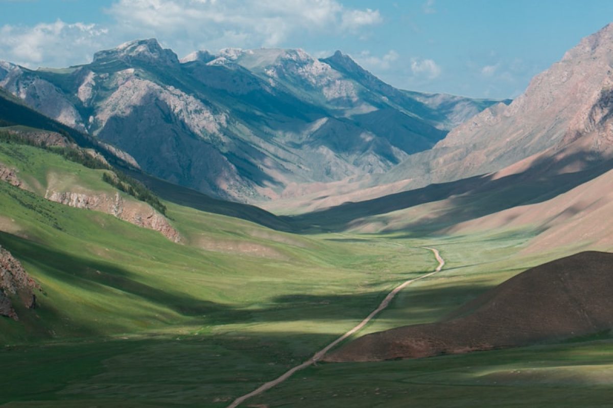 green grass field valley under white clouds during daytime