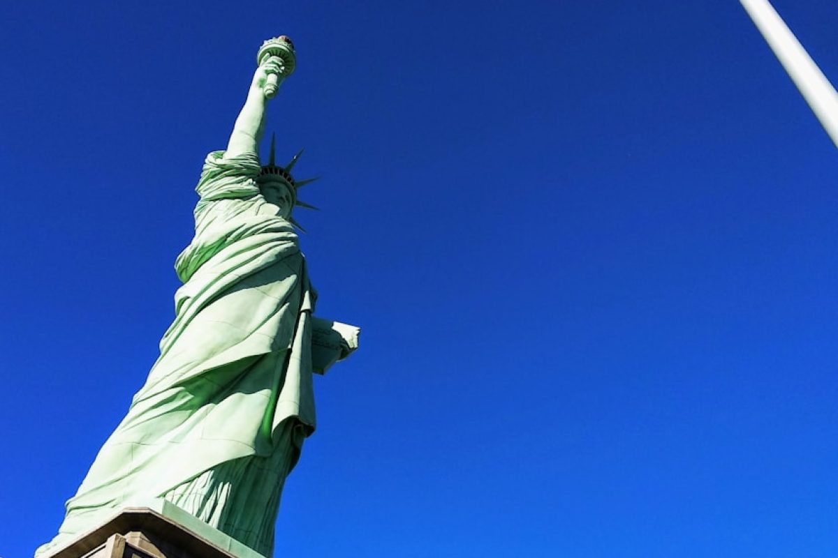 Statue of Liberty in front USA flag under blue sky