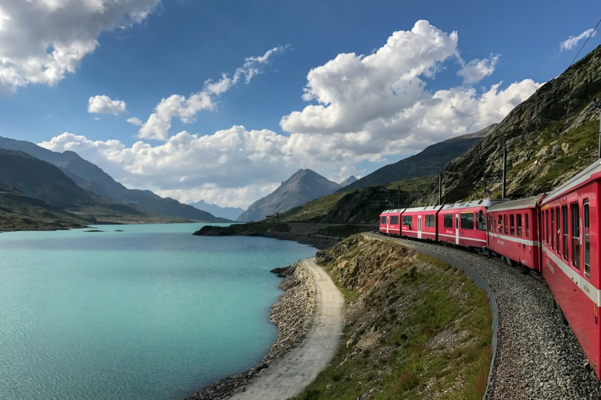 red train travelling near body of water