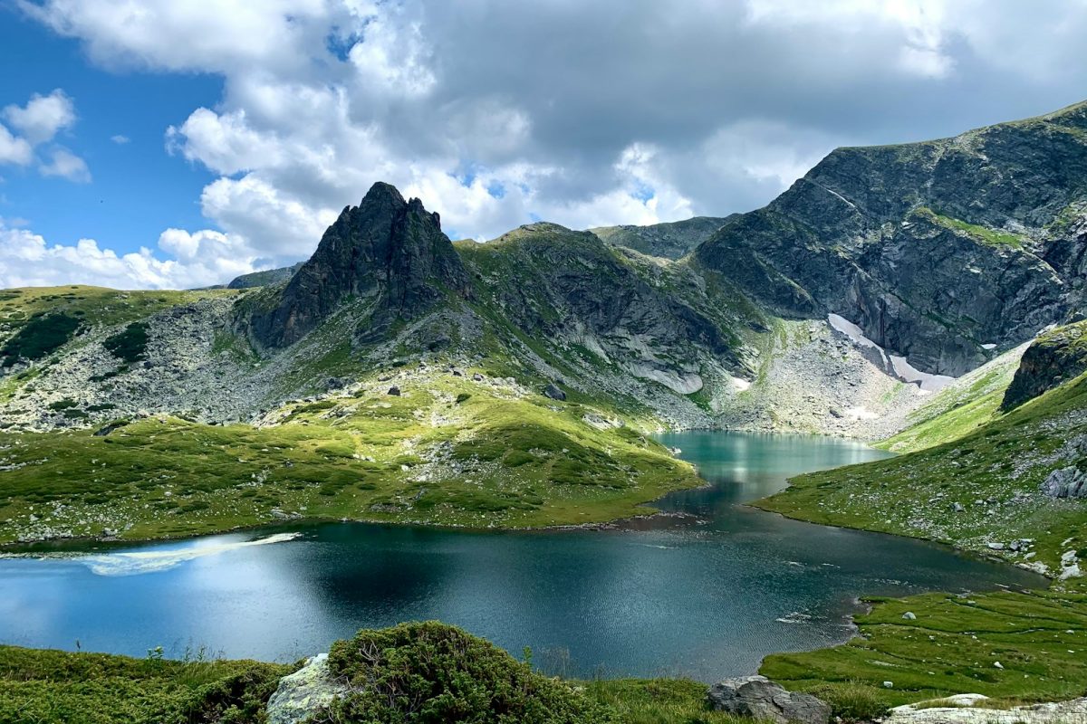 green and gray mountain near lake under white clouds and blue sky during daytime