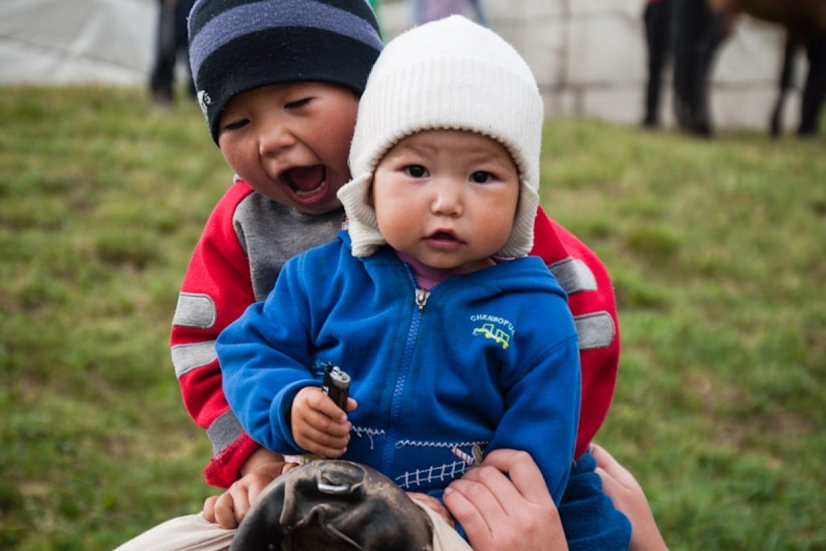 boy in blue jacket and white hat sitting on white and black horse during daytime